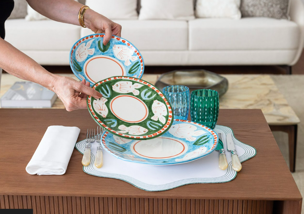 mulher montando uma mesa posta com pratos fazendo uma Sobreposição de pratos e sousplats com produtos da matisse casa